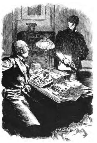 Man in dark clothes talking to man seated at desk