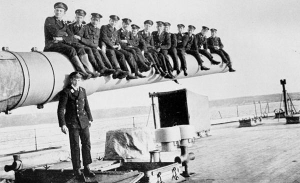 thirteen men sitting on top of large gun barrel
